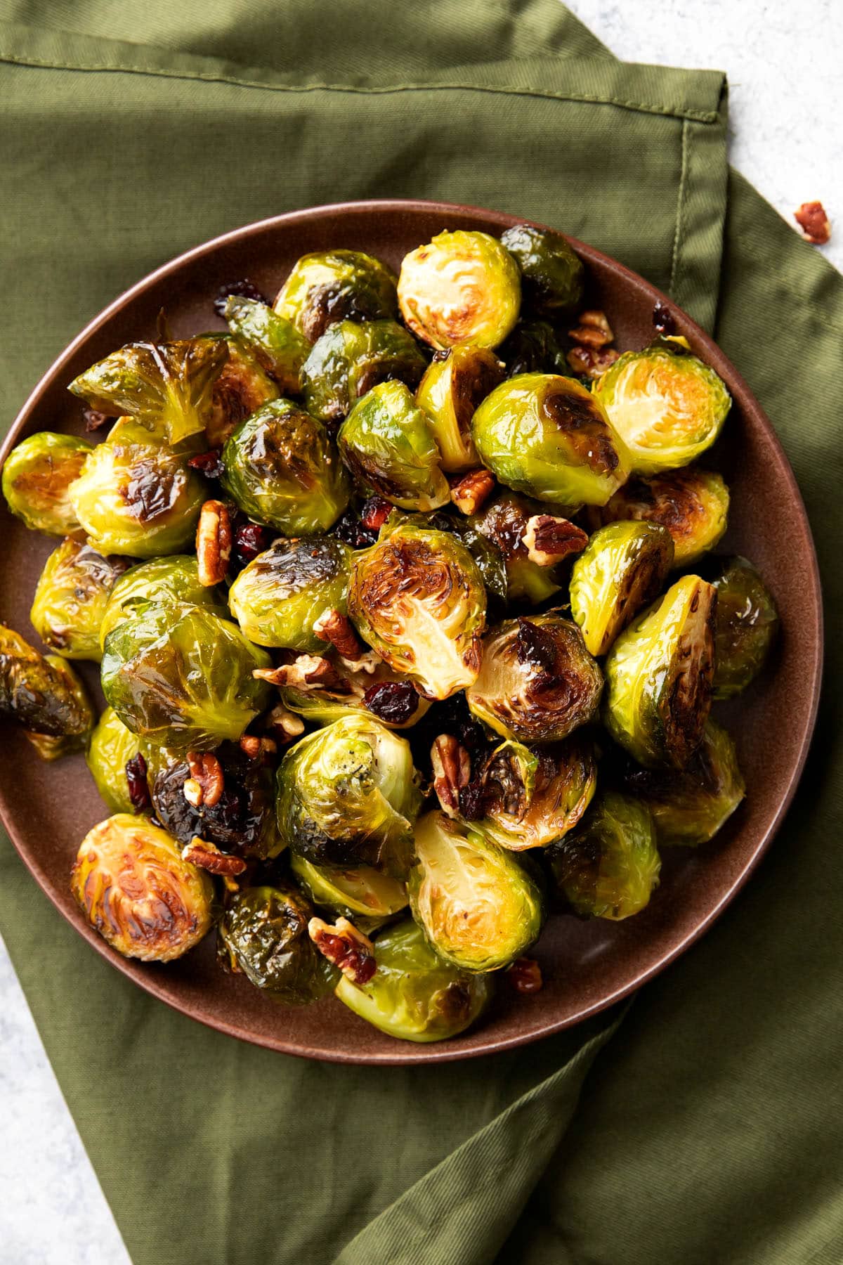 Perfectly roasted maple Brussel sprouts with maple syrup in a serving dish with cranberries, bacon, and almonds.