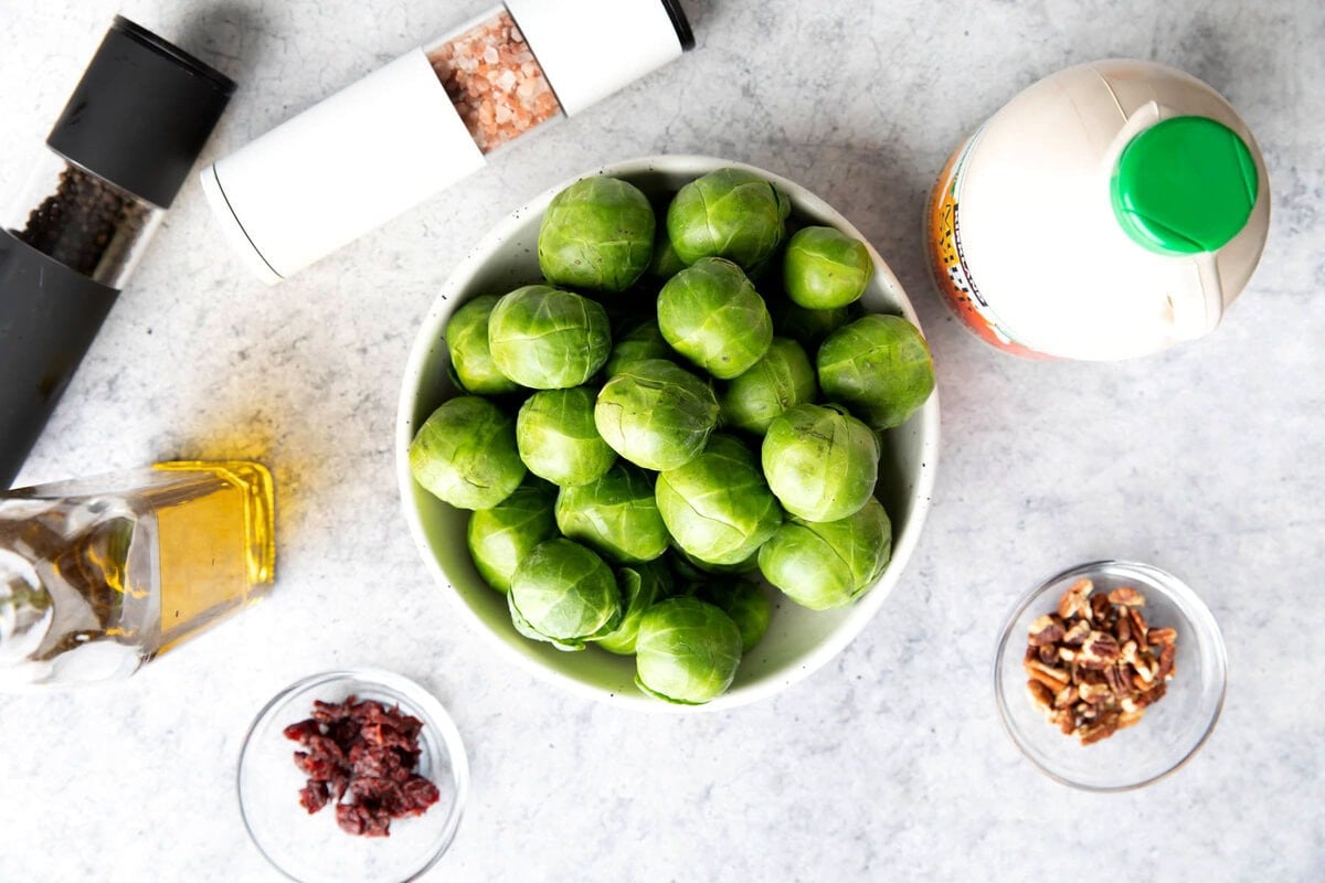 Maple glazed Brussel sprouts recipe ingredients in bowls including Brussels sprouts, maple syrup, oil, salt and pepper, bacon crumbles, almonds, and more.