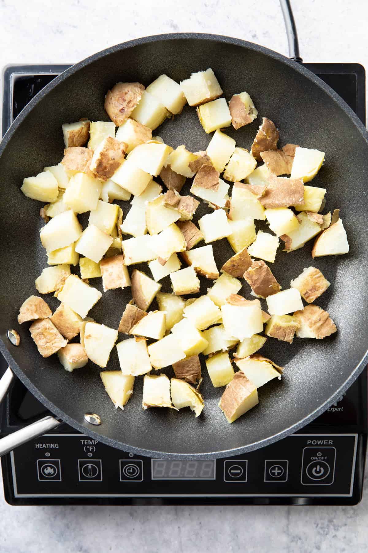 Chopped potatoes cooking on a nonstick skillet over heat 