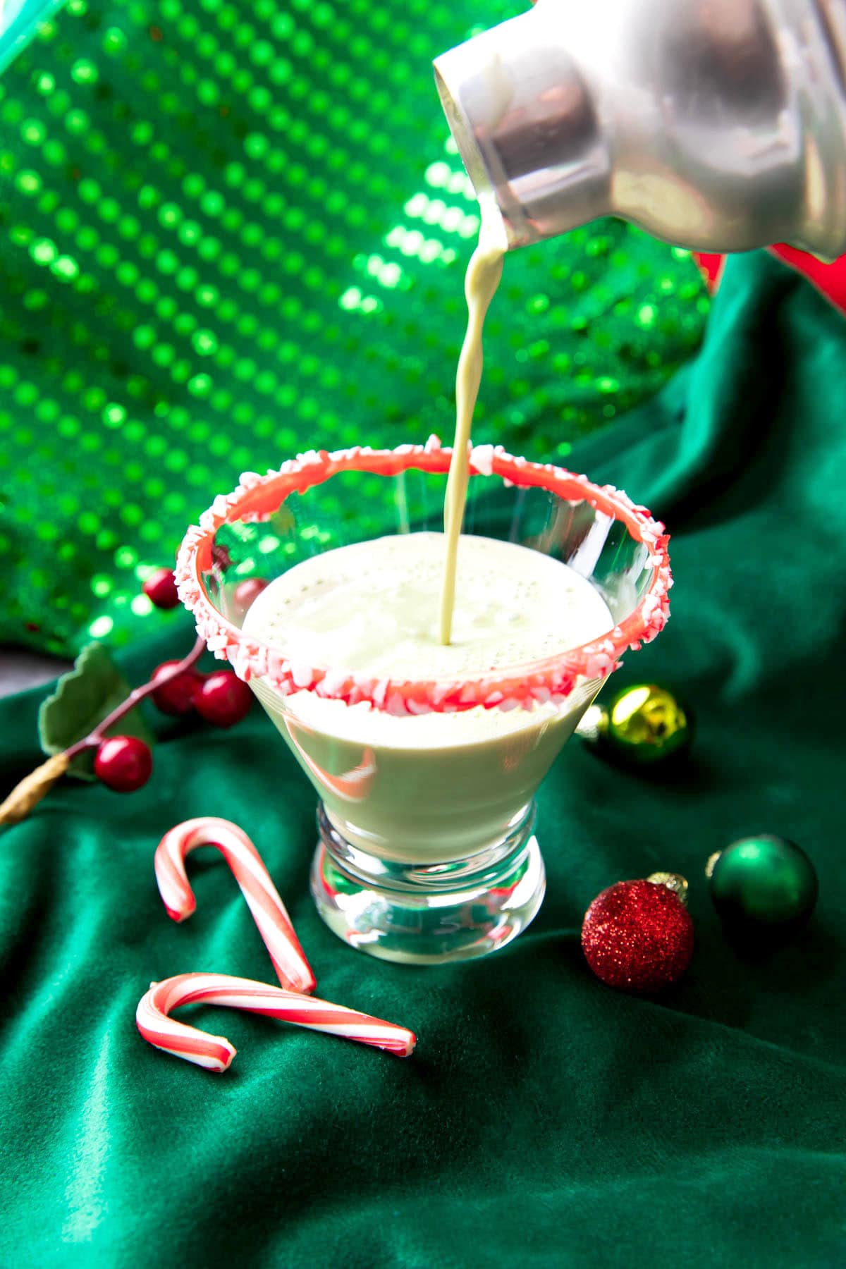 Someone straining peppermint martini mixture into a rimmed cocktail glass.