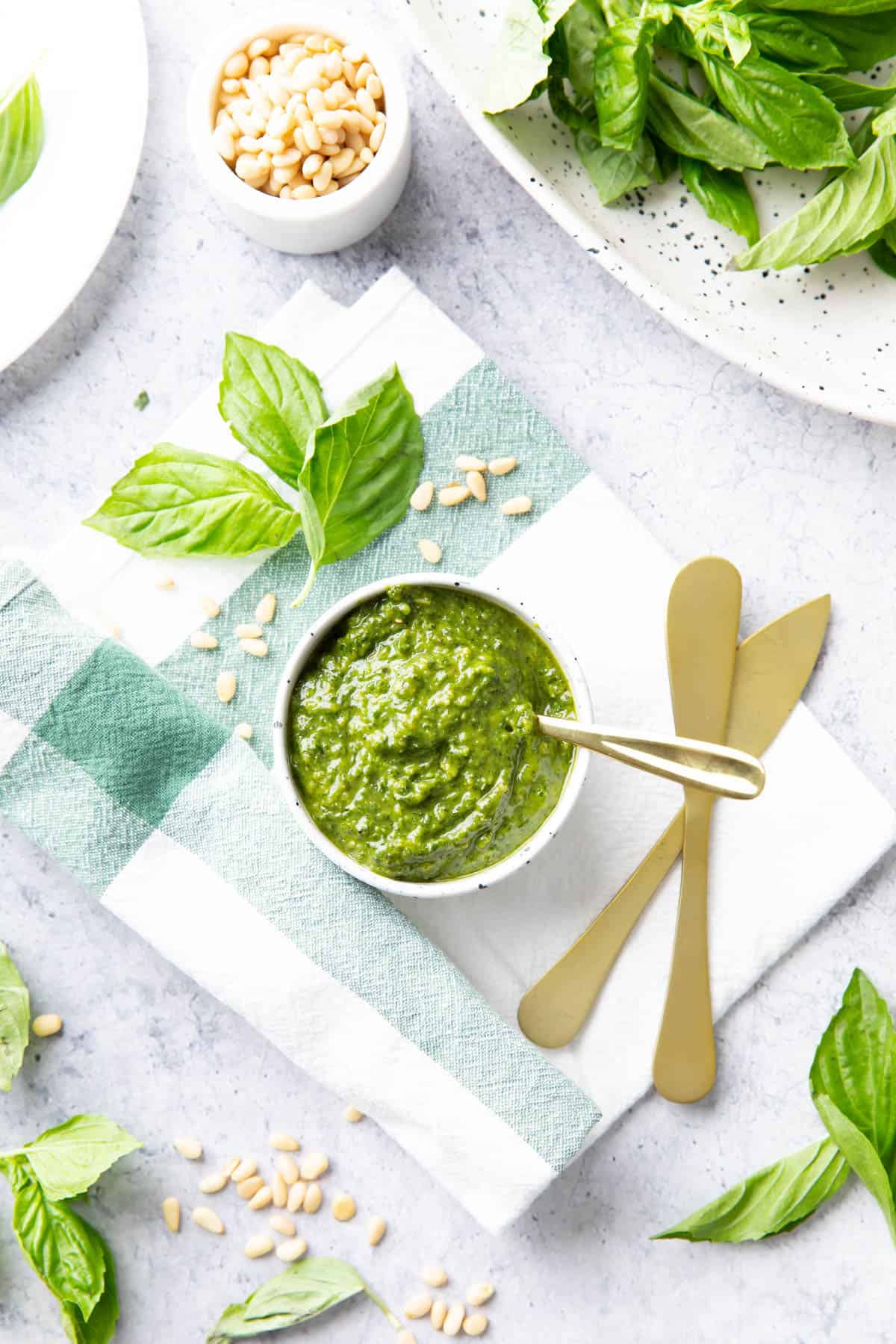 Kitchen table with vegan pesto, fresh basil, pine nuts, and kitchen tools 