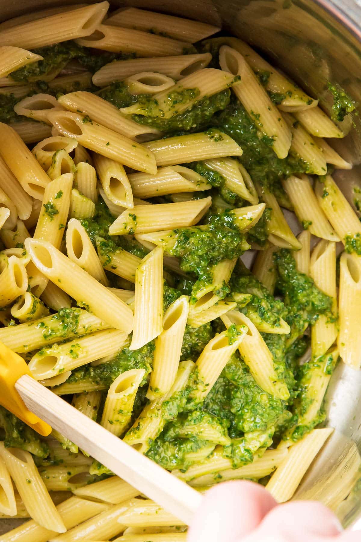 Someone coating penne pasta with basil pesto sauce before serving.