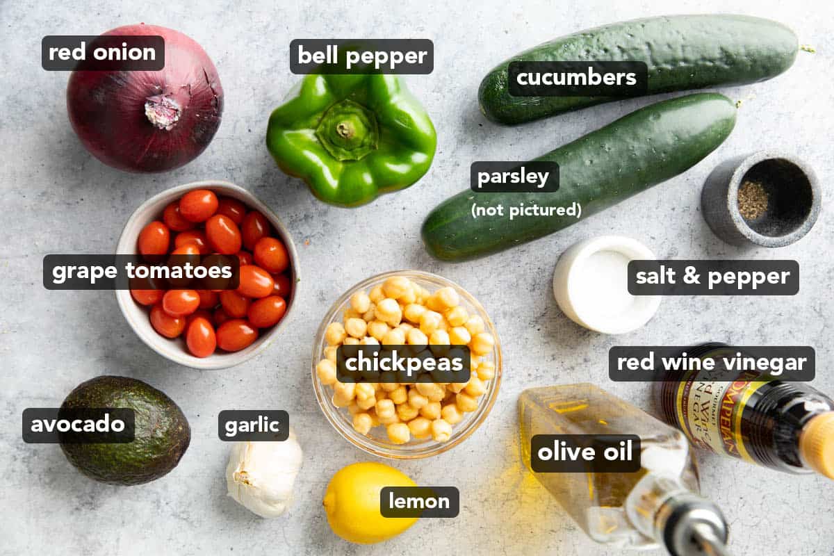 all ingredients for this chickpea salad recipe laid out: grape tomatoes, avocado, garlic, lemon, olive oil, red wine vinegar, salt & pepper, parsley, cucumbers, and bell pepper.