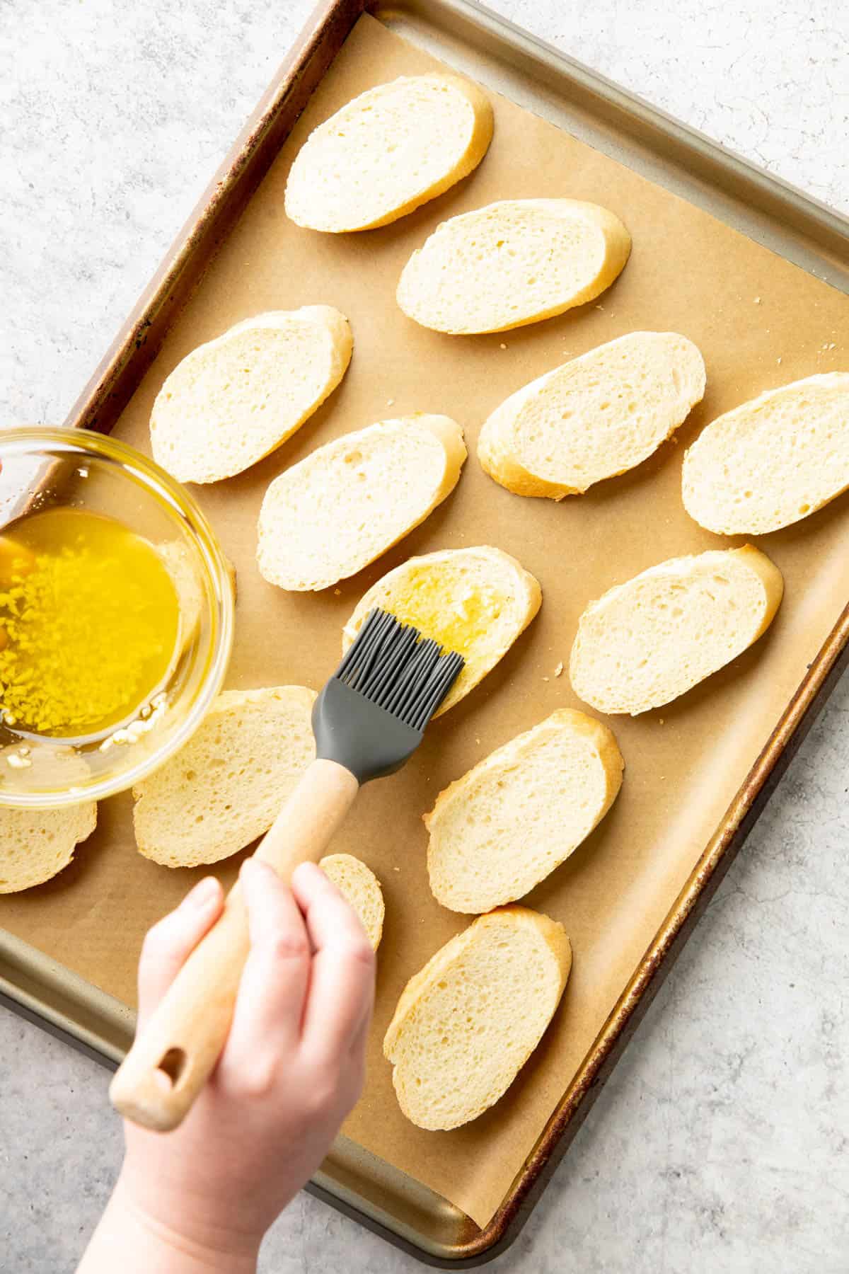 A hand brushing flavored oil onto baguette rounds