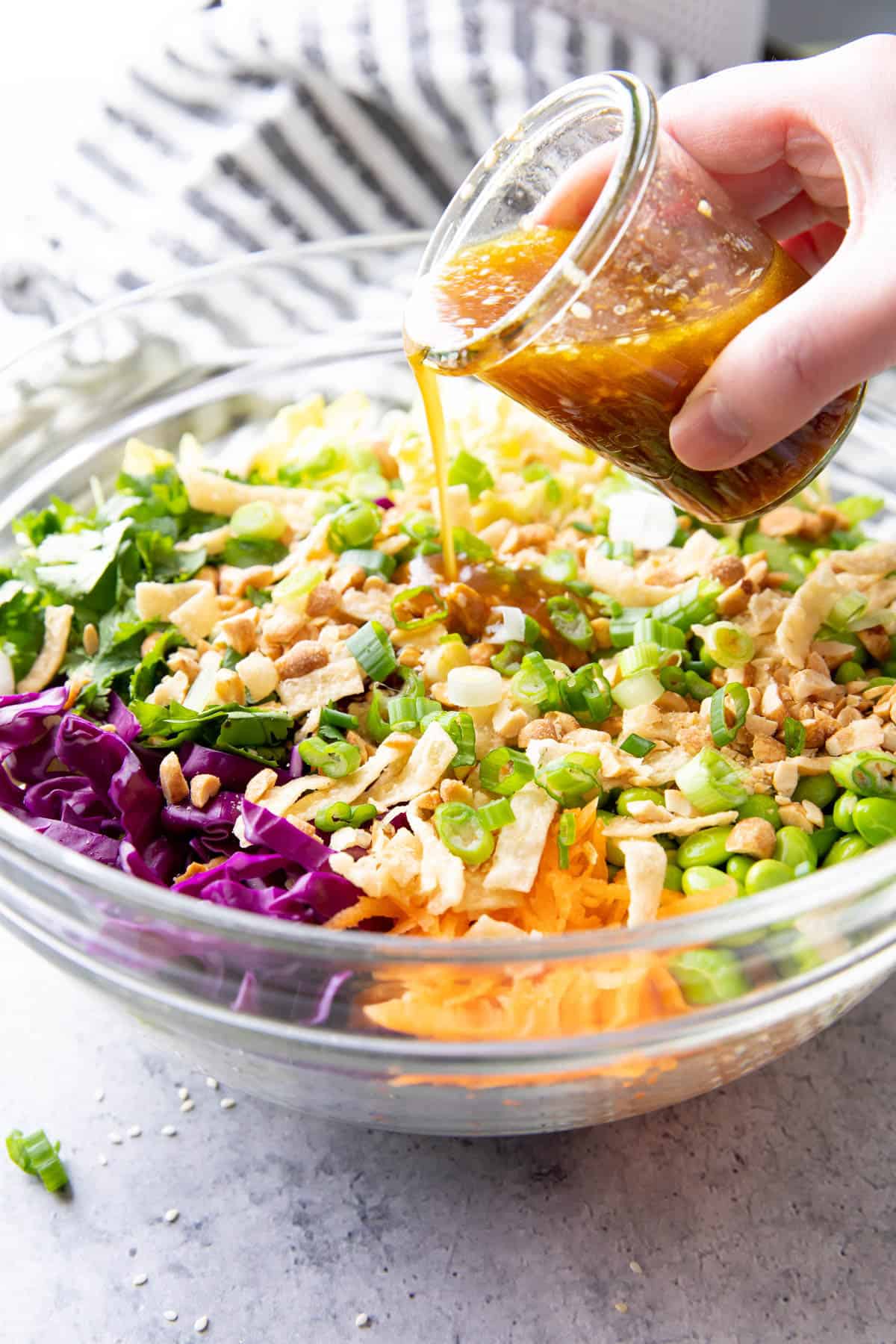 hand pouring jar of dressing over Asian Salad