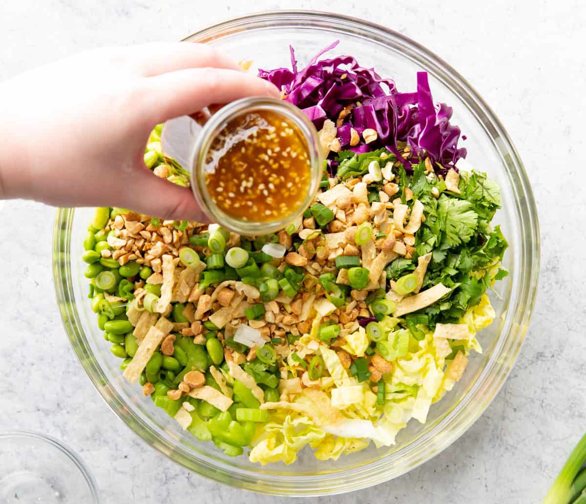 Dressing poured over bowl of chopped cabbage, green onions, edamame, wonton strips, peanuts