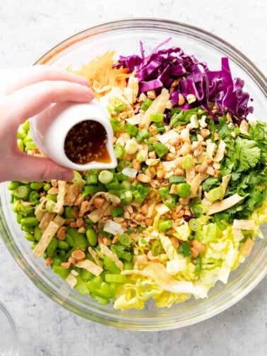 hand pouring white jar of dressing over chopped vegetables