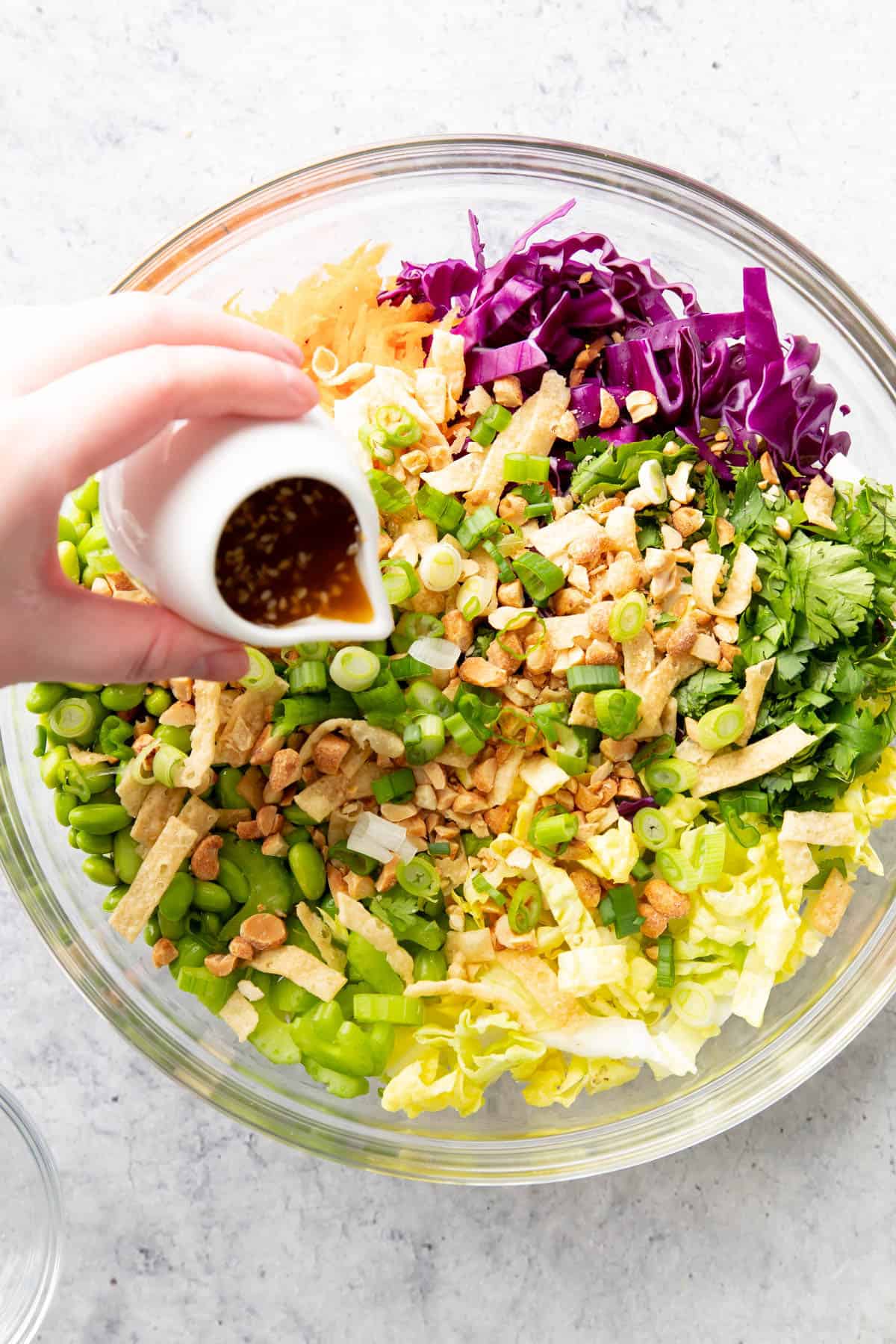 hand pouring white jar of dressing over chopped vegetables