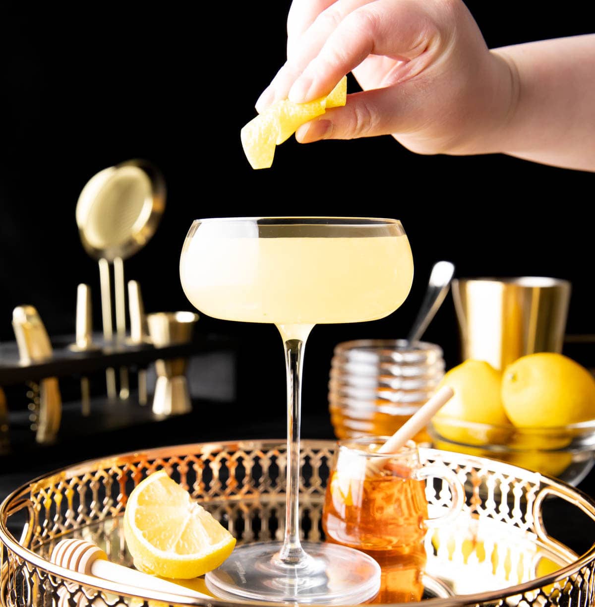 A photo showing How to make a Bee’s Knees Cocktail – expressing oil out of lemon garnish into glass