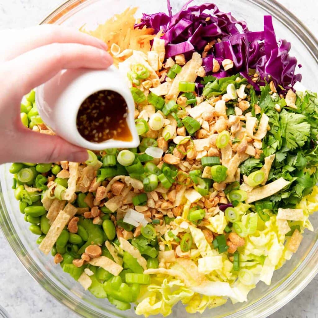hand pouring dressing over Asian Salad in salad bowl