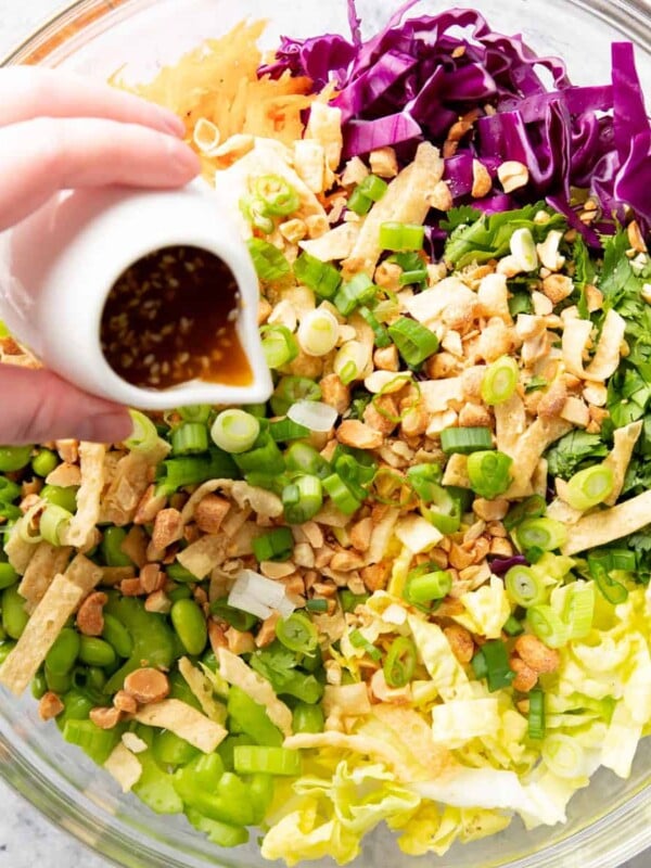 hand pouring dressing over Asian Salad in salad bowl