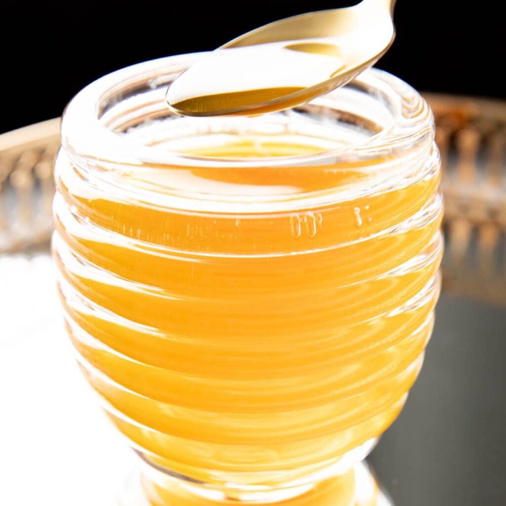 Honey syrup dripping from a spoon into its jar