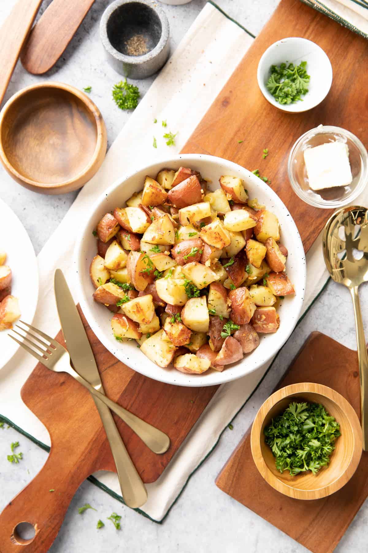 dining table with garlic parmesan roasted potatoes in a serving bowl with butter, salt, and pepper