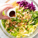 pouring salad dressing over salad in glass bowl