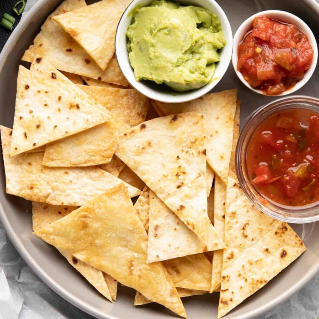 Baked tortilla chips on a plate with salsa and guacamole.