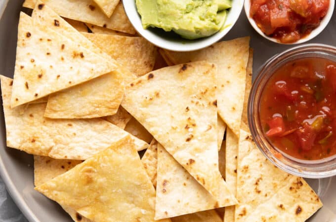 Baked tortilla chips on a plate with salsa and guacamole.