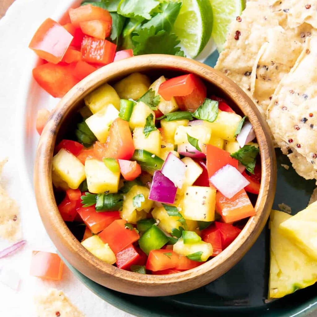 Dipping bowl filled with pineapple salsa served with tortilla chips and lime wedges