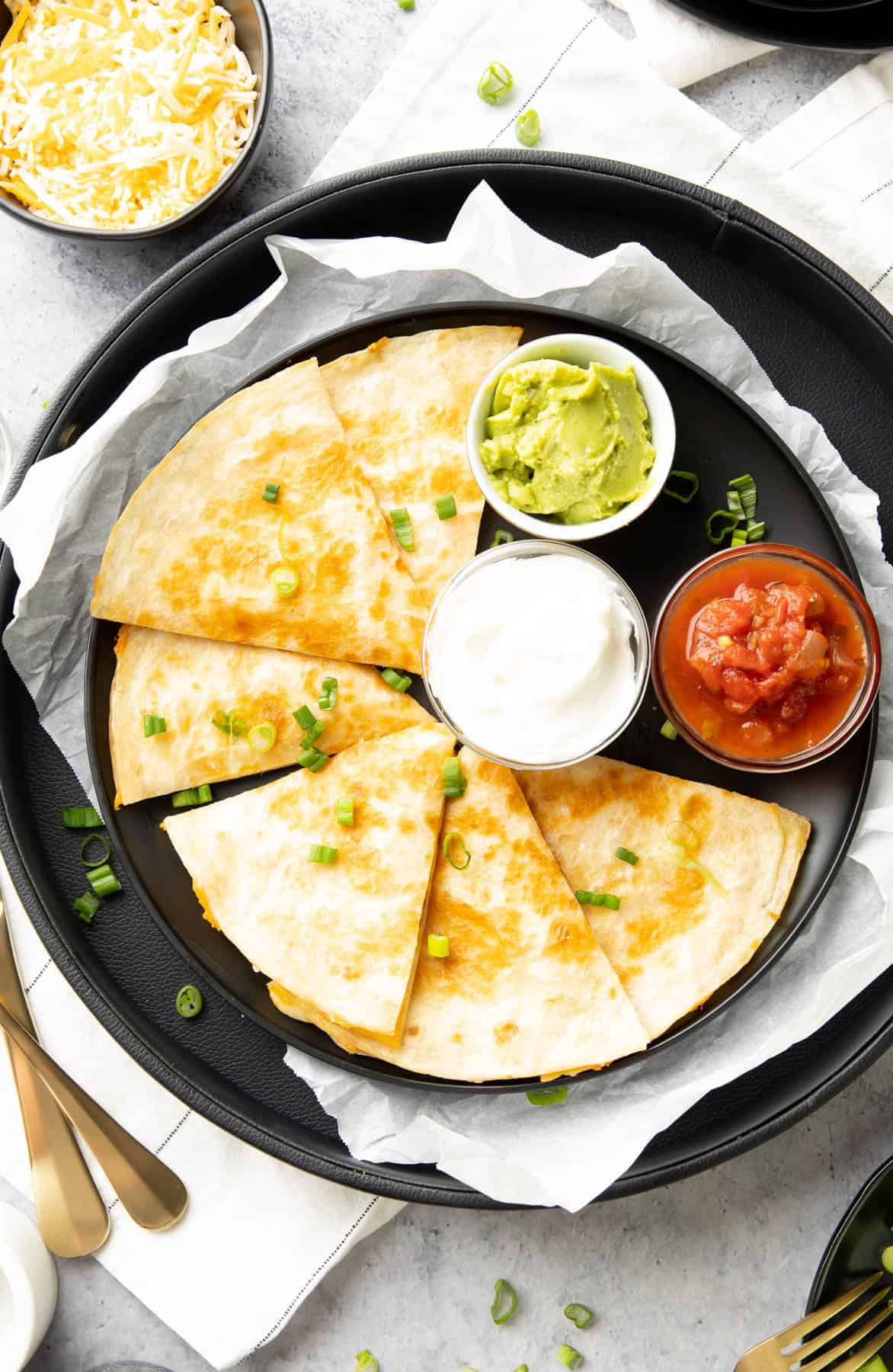 slices of cheese quesadilla served on a plate with guacamole, salsa, and sour cream