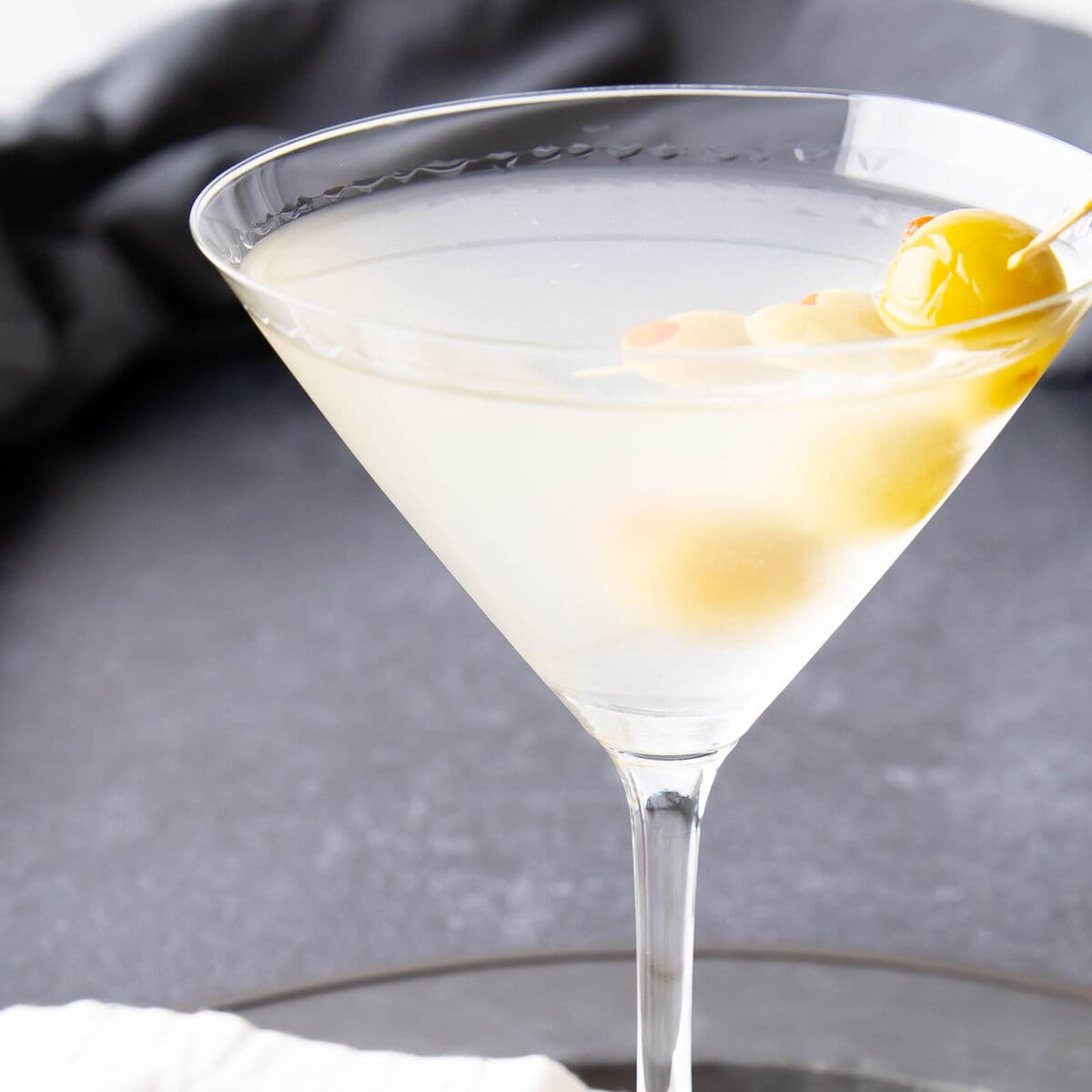 Dirty Martini served in a chilled glass with an olive skewer against a gray backdrop