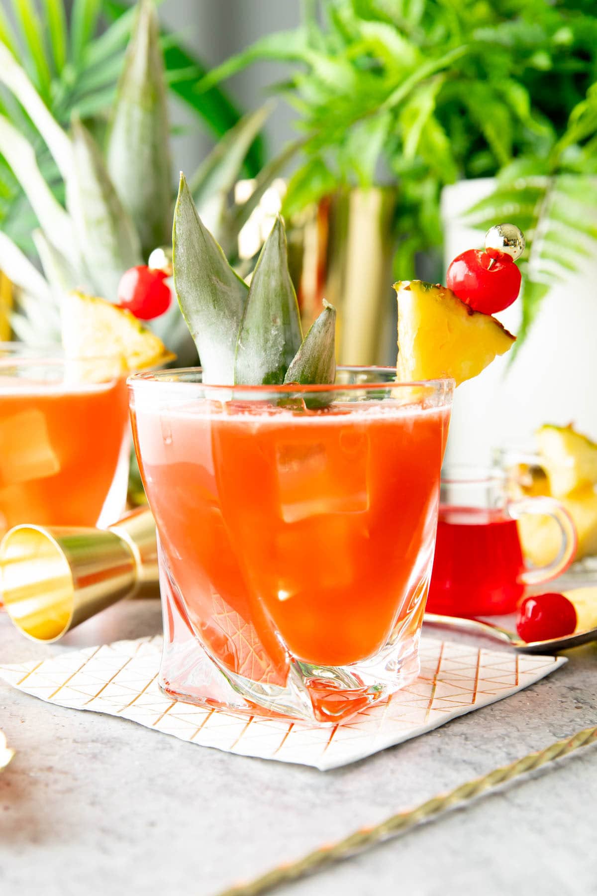 Tropical pineapple rum drink served with maraschino cherry syrup, a cocktail set and palm leaves