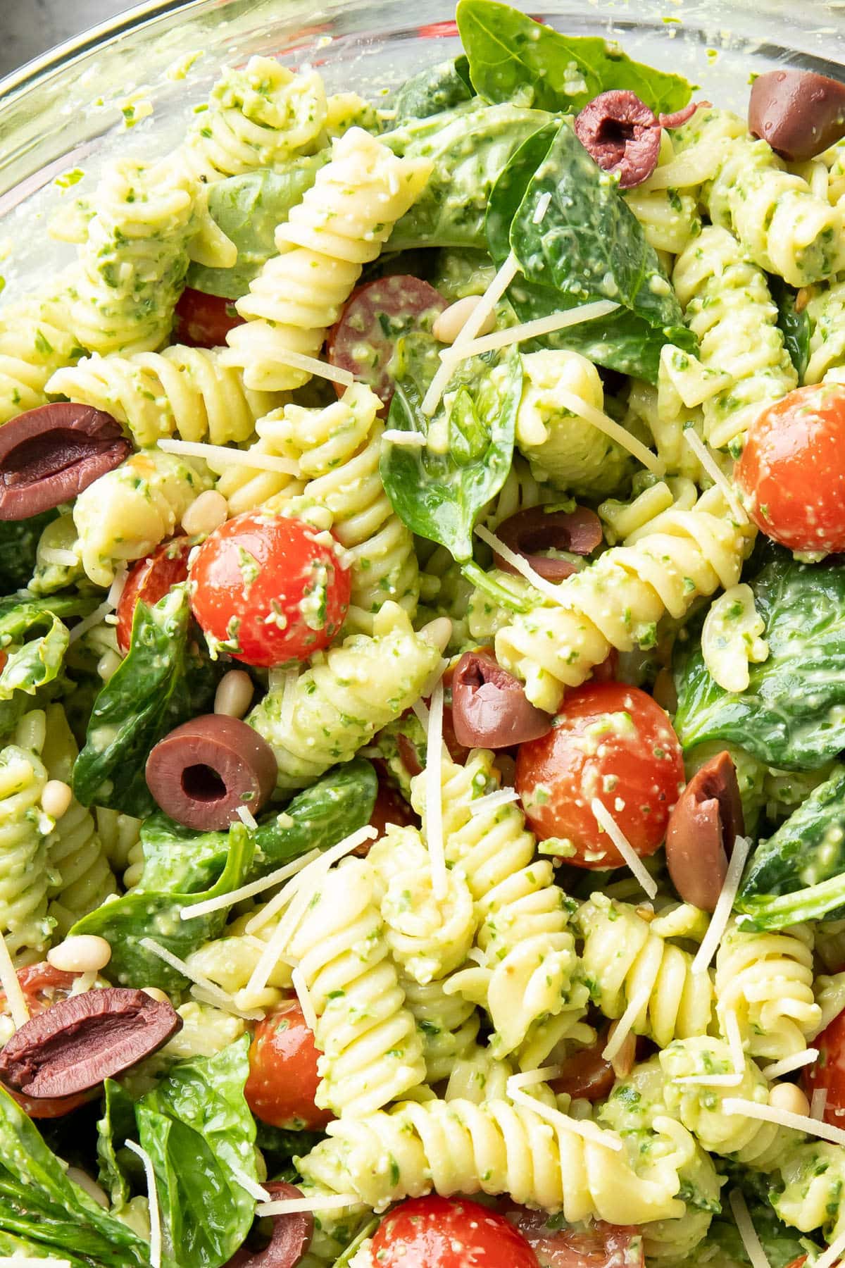 close up creamy pesto coating pasta in mixing bowl