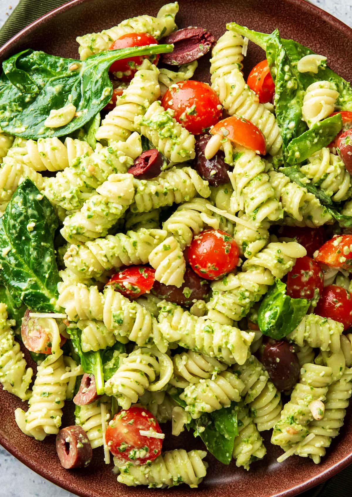 Close up of pesto pasta salad with feta cheese, homemade pesto sauce, cooked pasta, pine uts and spinach.