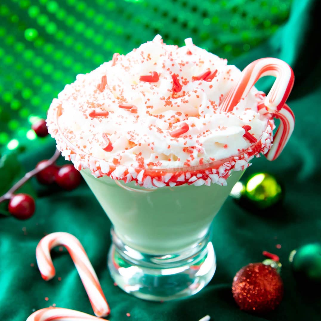 Peppermint Martini topped with whipped cream and candy canes against a green backdrop