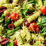 Close up of Spinach Pesto Pasta Salad shows pasta, tomatoes, lots of pesto sauce, basil leaves and feta cheese