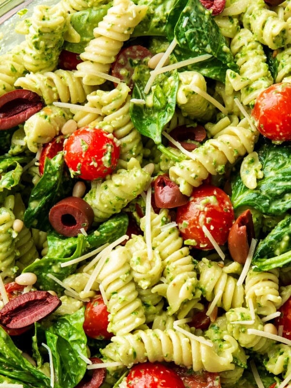 Close up of Spinach Pesto Pasta Salad shows pasta, tomatoes, lots of pesto sauce, basil leaves and feta cheese