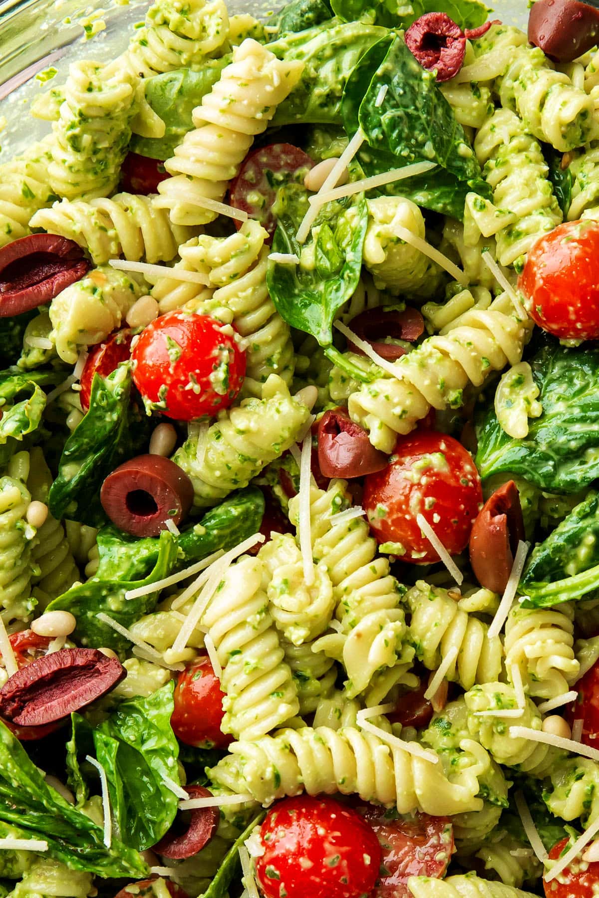 Close up of Spinach Pesto Pasta Salad shows pasta, tomatoes, lots of pesto sauce, basil leaves and feta cheese.