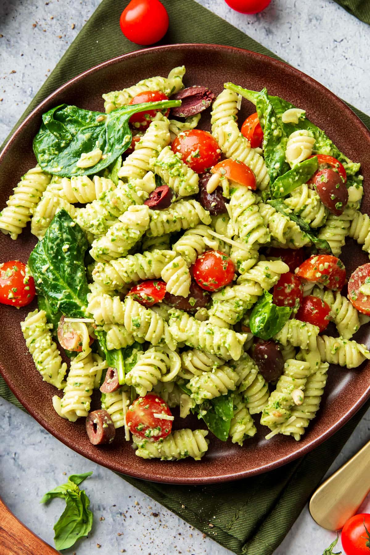 This pesto pasta salad is served on a plate with olives, spinach and feta.