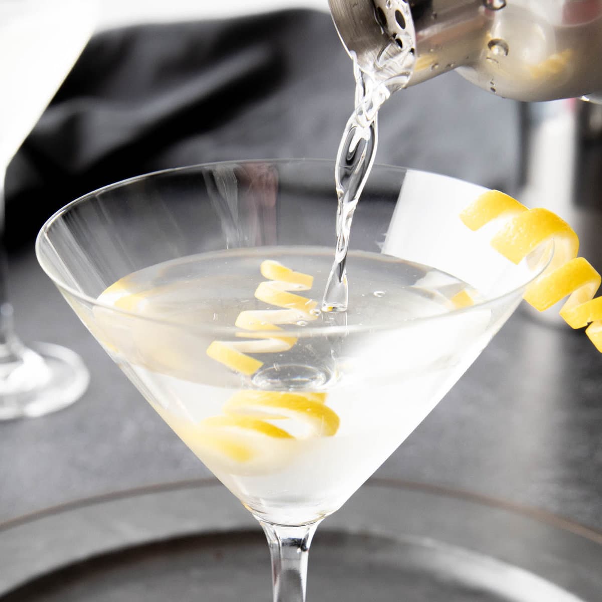 Pouring martini mixture from cocktail shaker into chilled martini glass