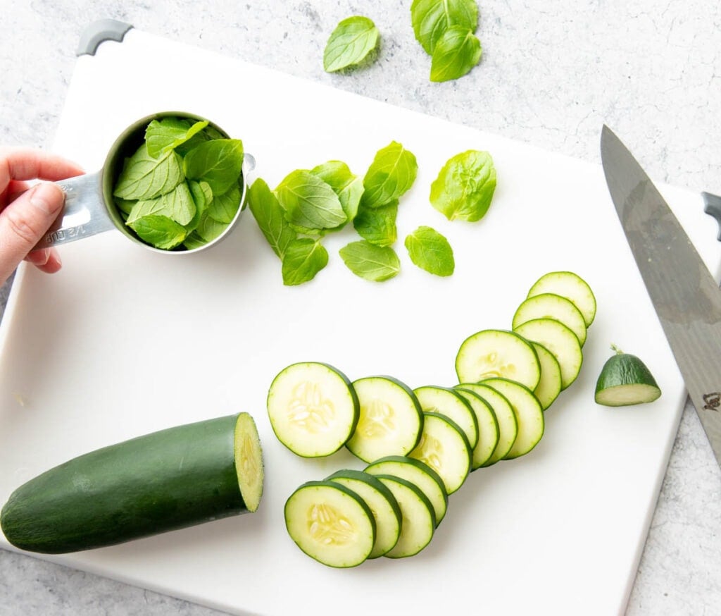 A photo showing How to Make Cucumber Water – slicing cucumbers on a cutting board