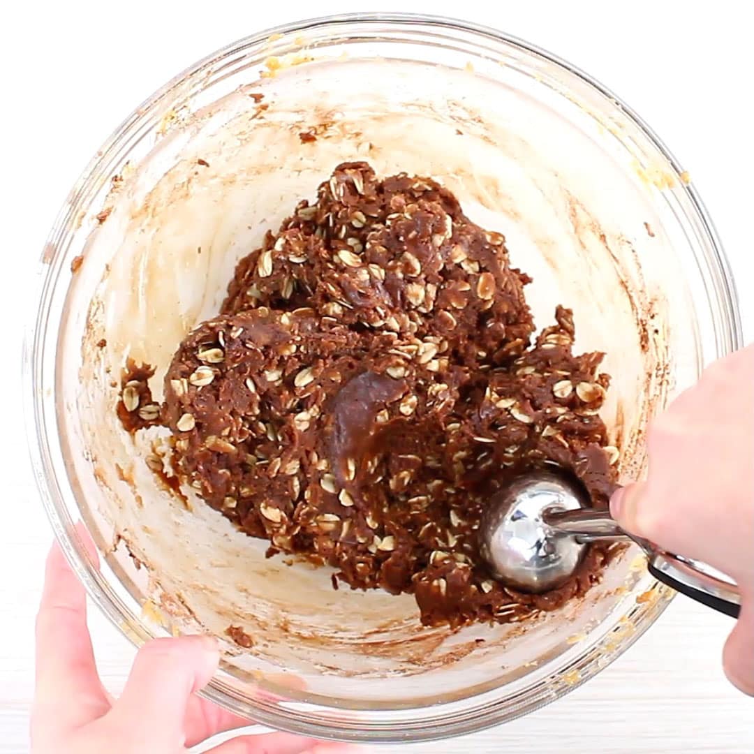 Using a cookie scoop to scoop cookie dough onto a lined baking sheet