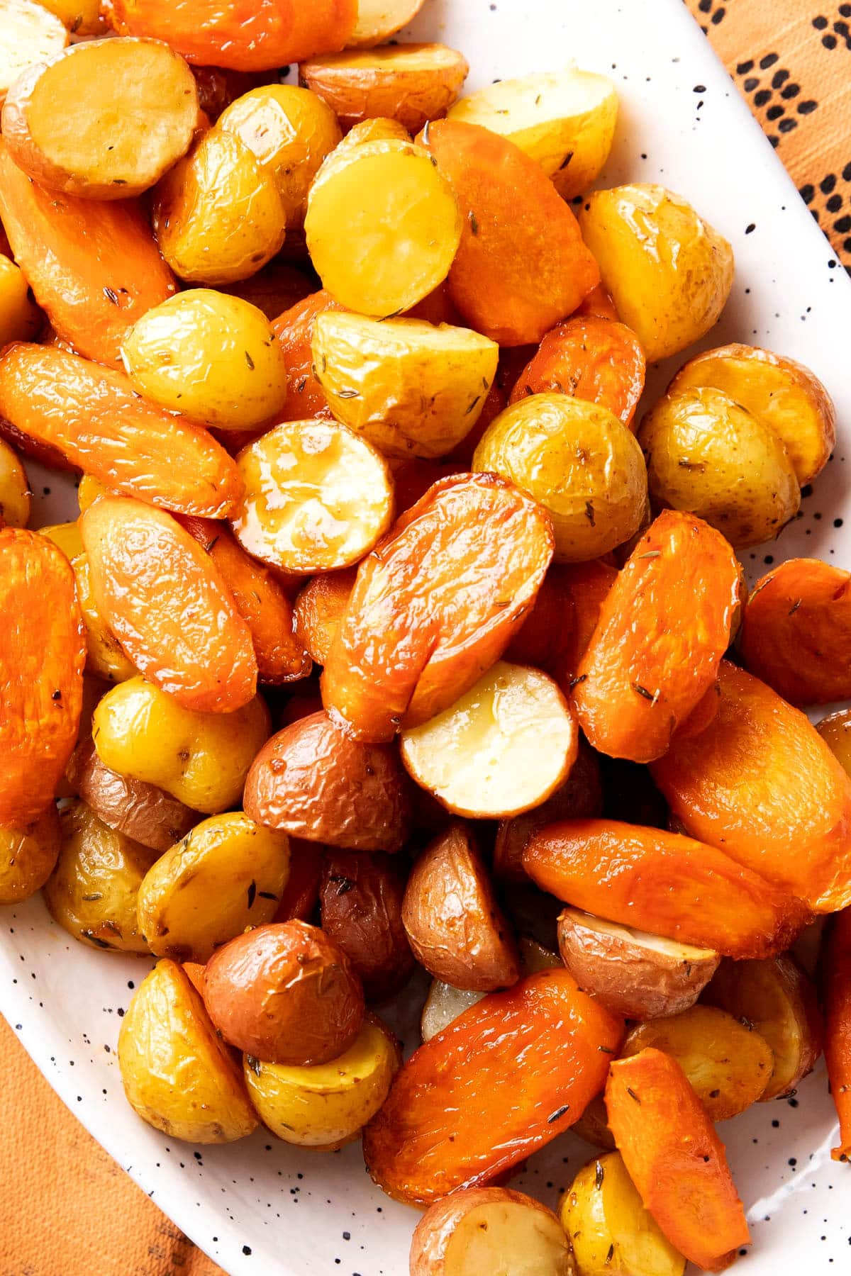 close up of roasted carrots and potatoes to show butter, herbs, and other seasonings that coat this recipe