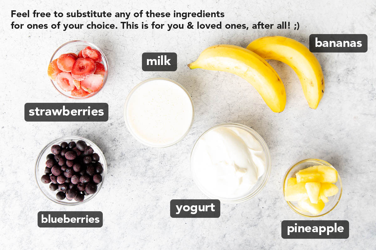 Berry Pineapple Smoothie ingredients on a table including blueberries, pineapples, yogurt, milk, and strawberries