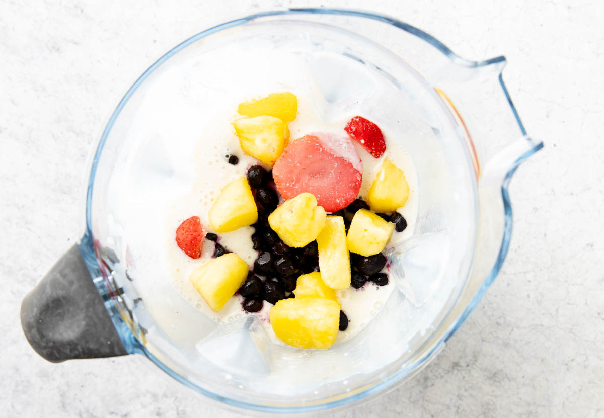 Adding berries into a blender to make a berry pineapple smoothie