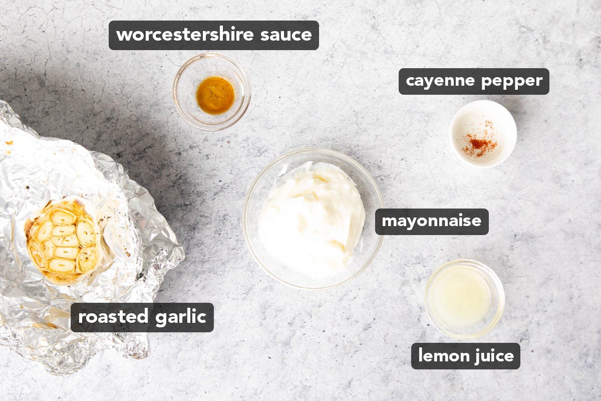 Roasted garlic aioli ingredients in glass bowls, including roasted garlic, mayonnaise, lemon juice, Worcestershire sauce, and cayenne pepper