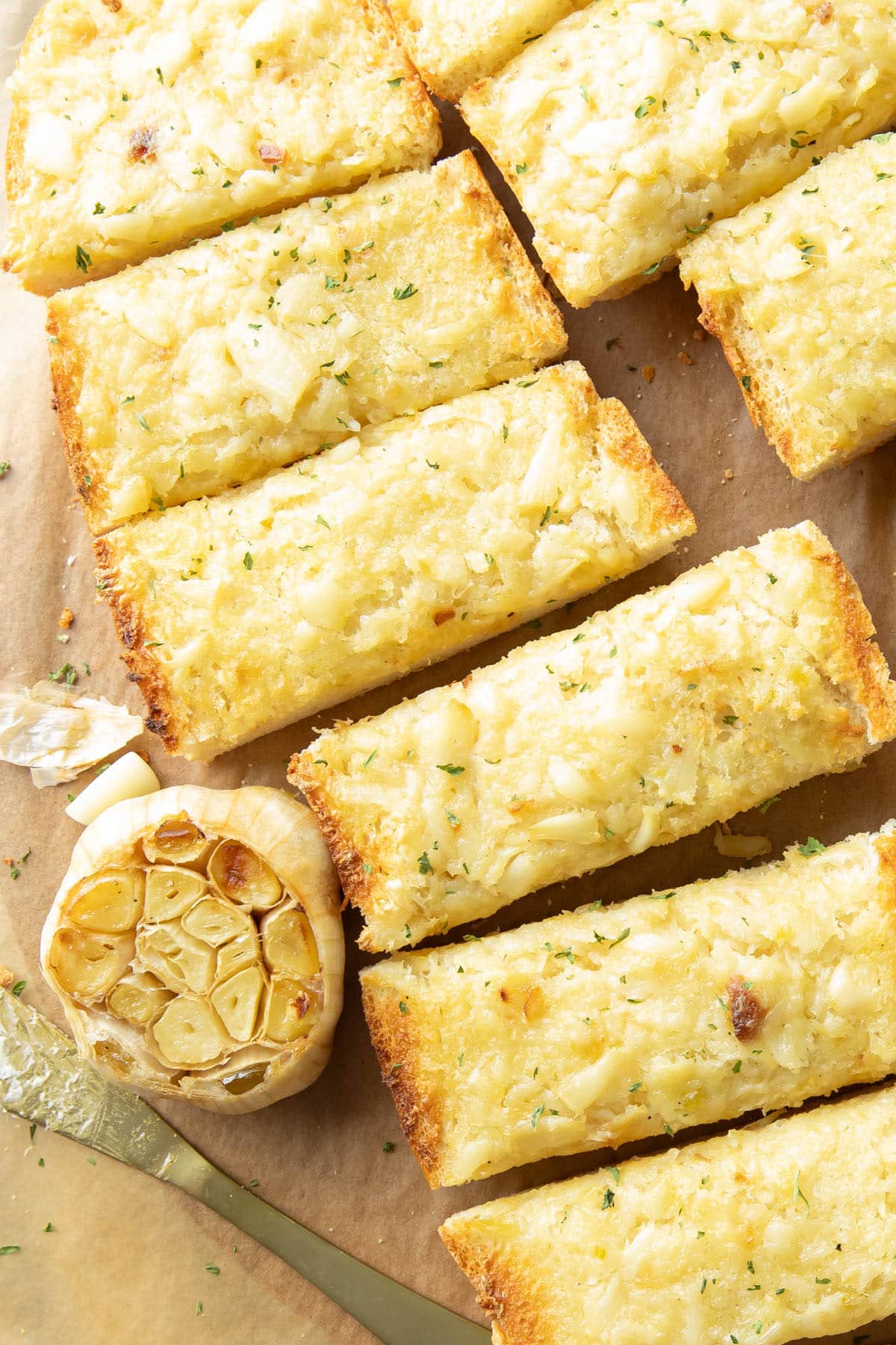 Slices of Garlic Bread fanned out on a serving tray with a head of roasted garlic and a spreading knife