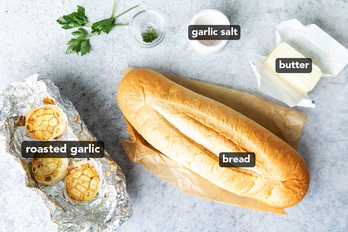 Roasted garlic bread recipe ingredients include a loaf of bread, butter, roasted garlic, salt, and parsley.