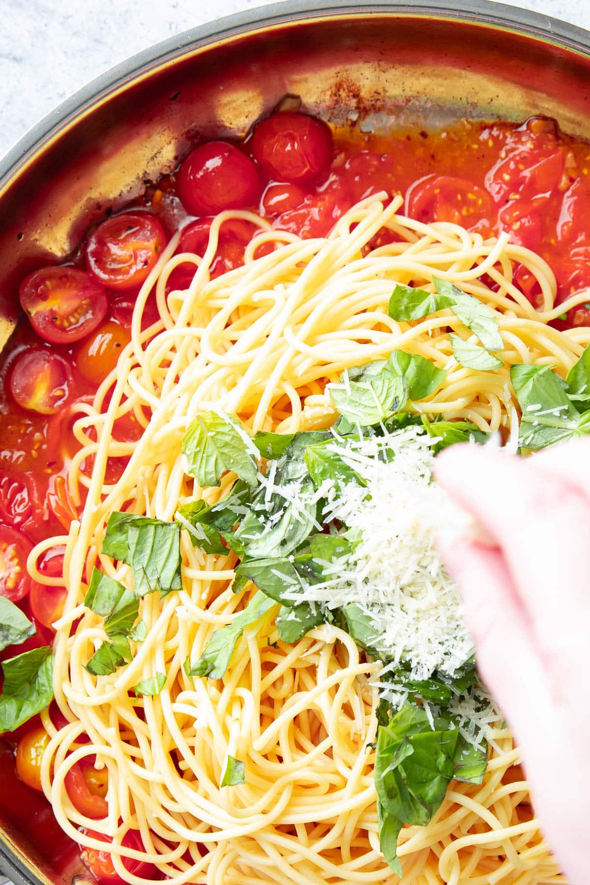 close up of hand sprinkling parmesan over tomato basil pasta