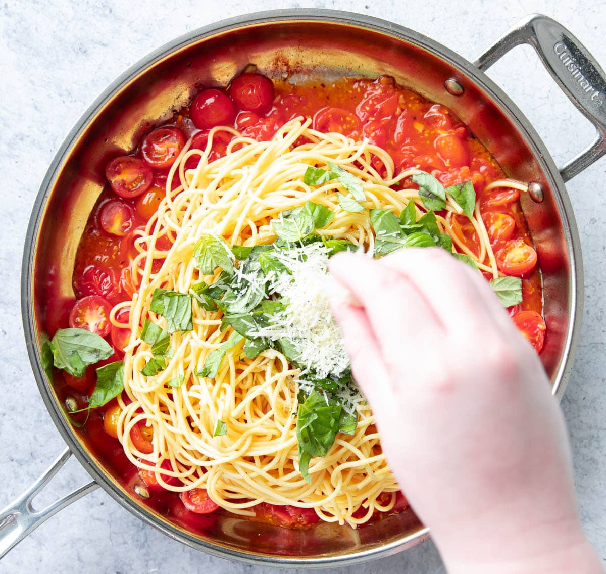 Hand sprinkling parmesan over fresh basil and spaghetti over tomato basil pasta