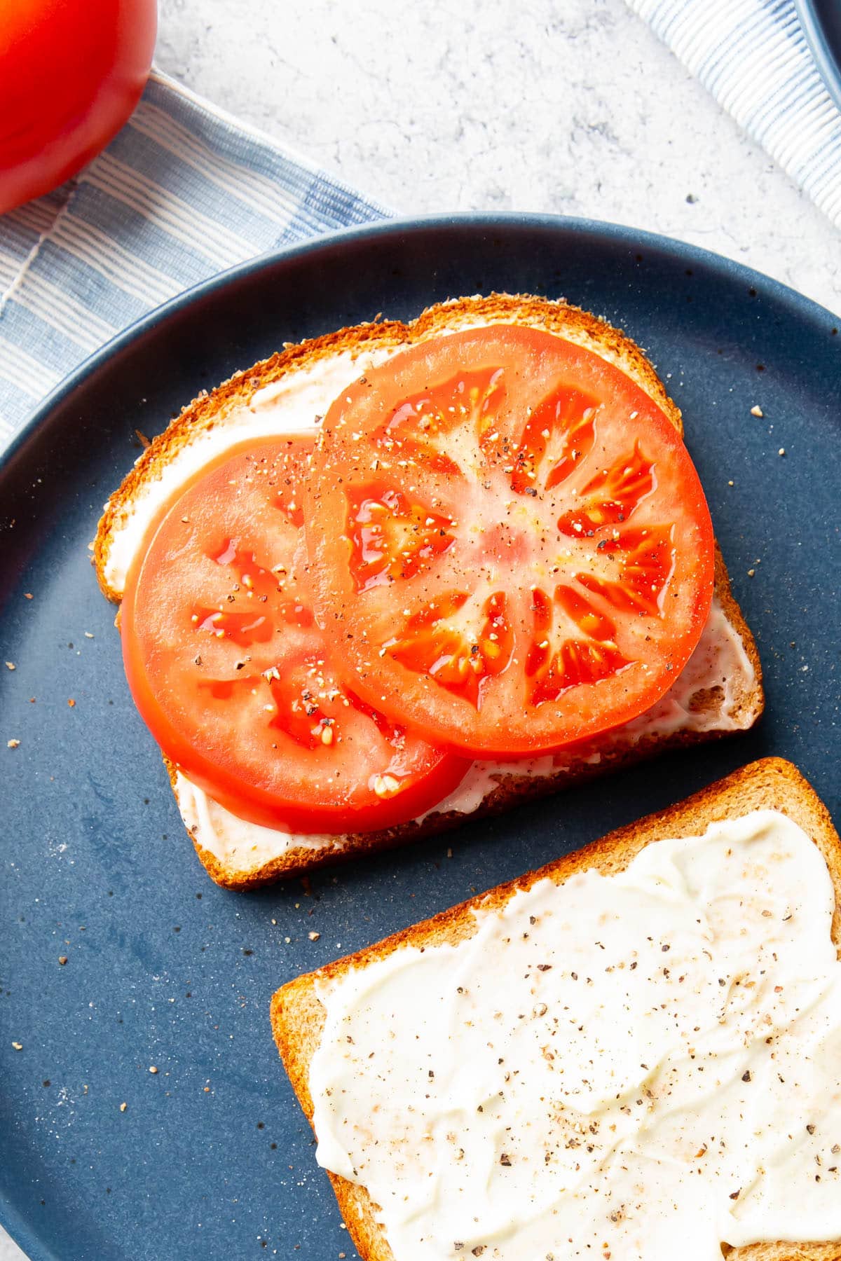 close up of beefsteak tomatoes atop Tomato Sandwich on a blue plate