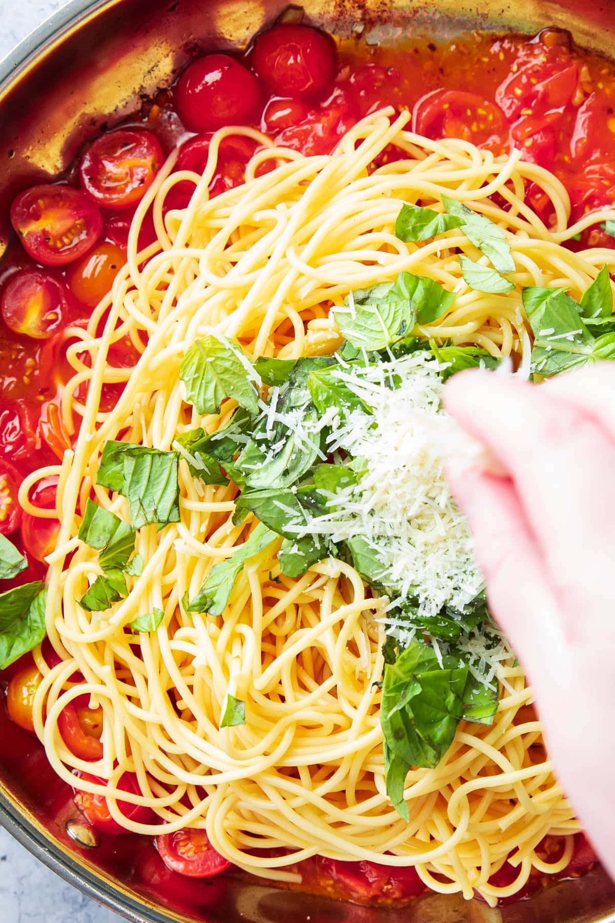 close up of hand sprinkling parmesan over tomato basil pasta