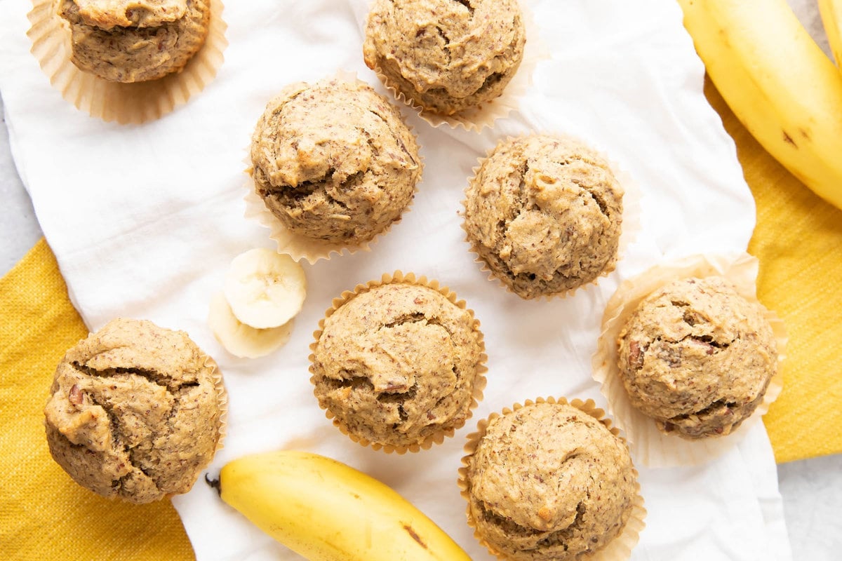 Fresh baked healthy banana muffins cooling on a kitchen towel with bananas