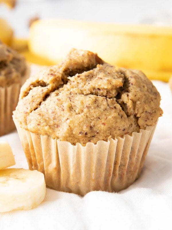 a single healthy banana muffin wrapped in a parchment muffin cup with banana slices