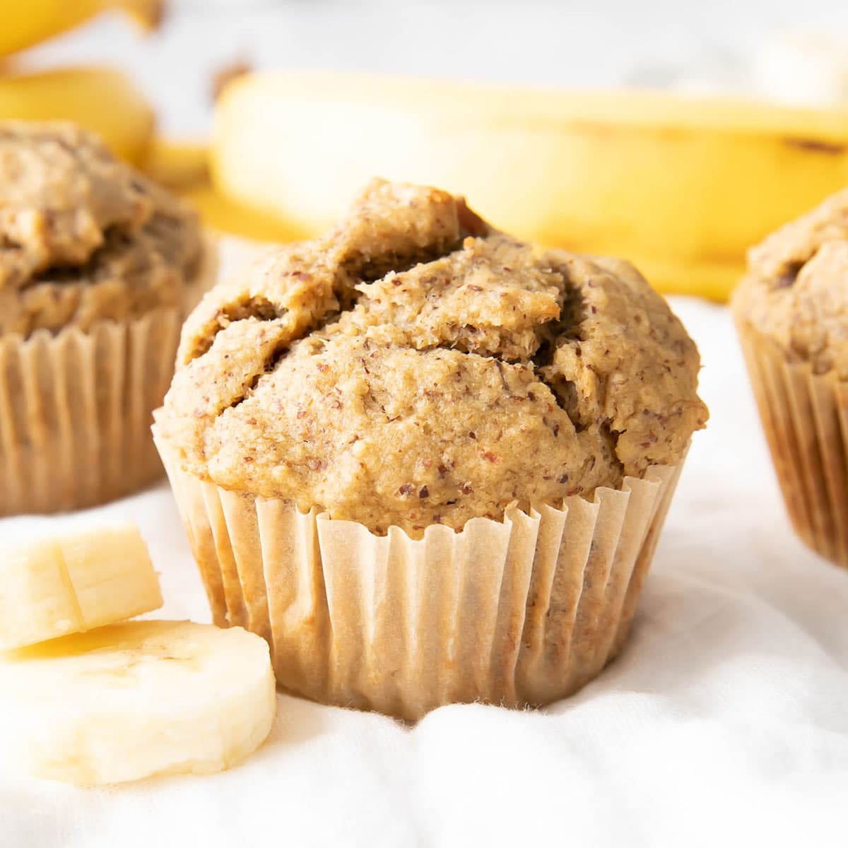 a single healthy banana muffin wrapped in a parchment muffin cup with banana slices