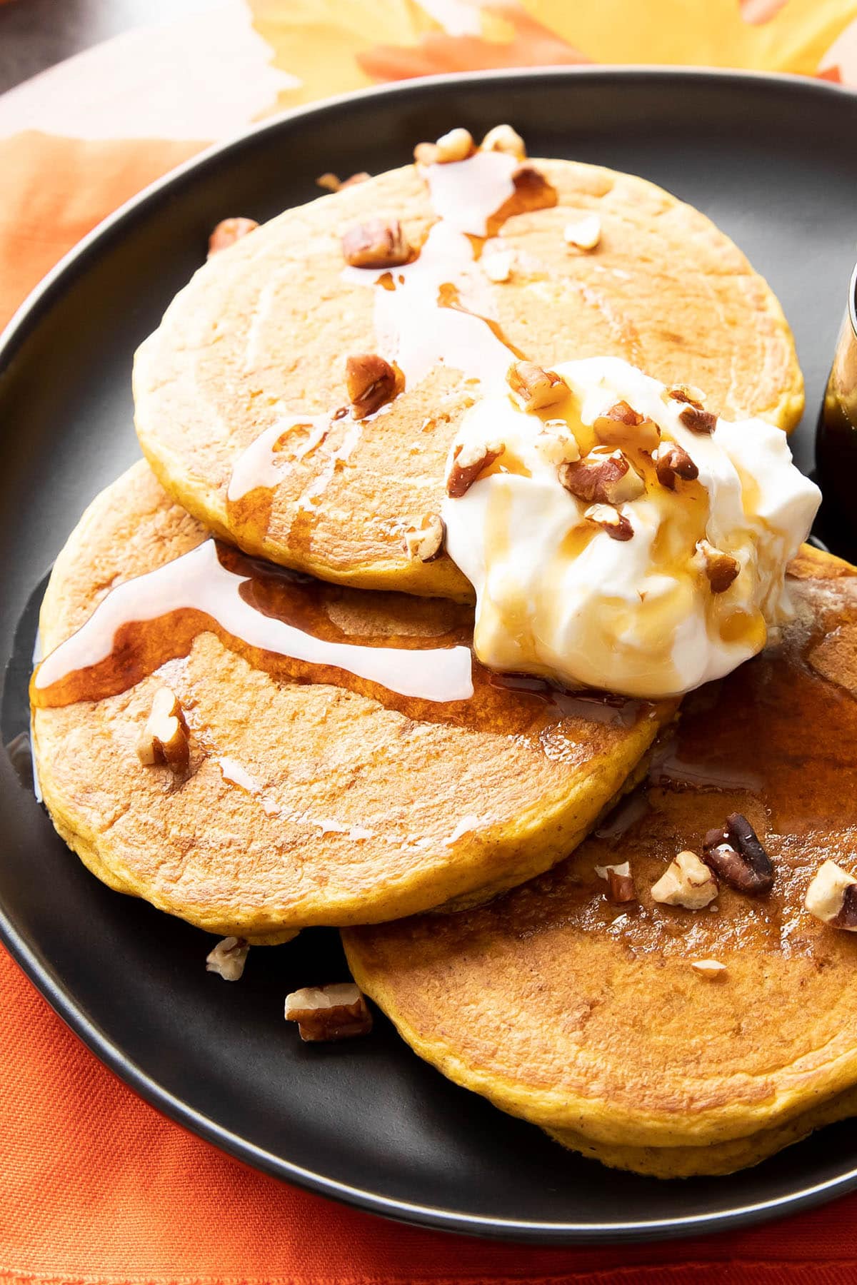 Close up of three pumpkin pancakes topped with pecans, syrup, and whipped topping