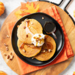 A plate full of pumpkin pancakes covered in syrup, whipped topping, and nuts