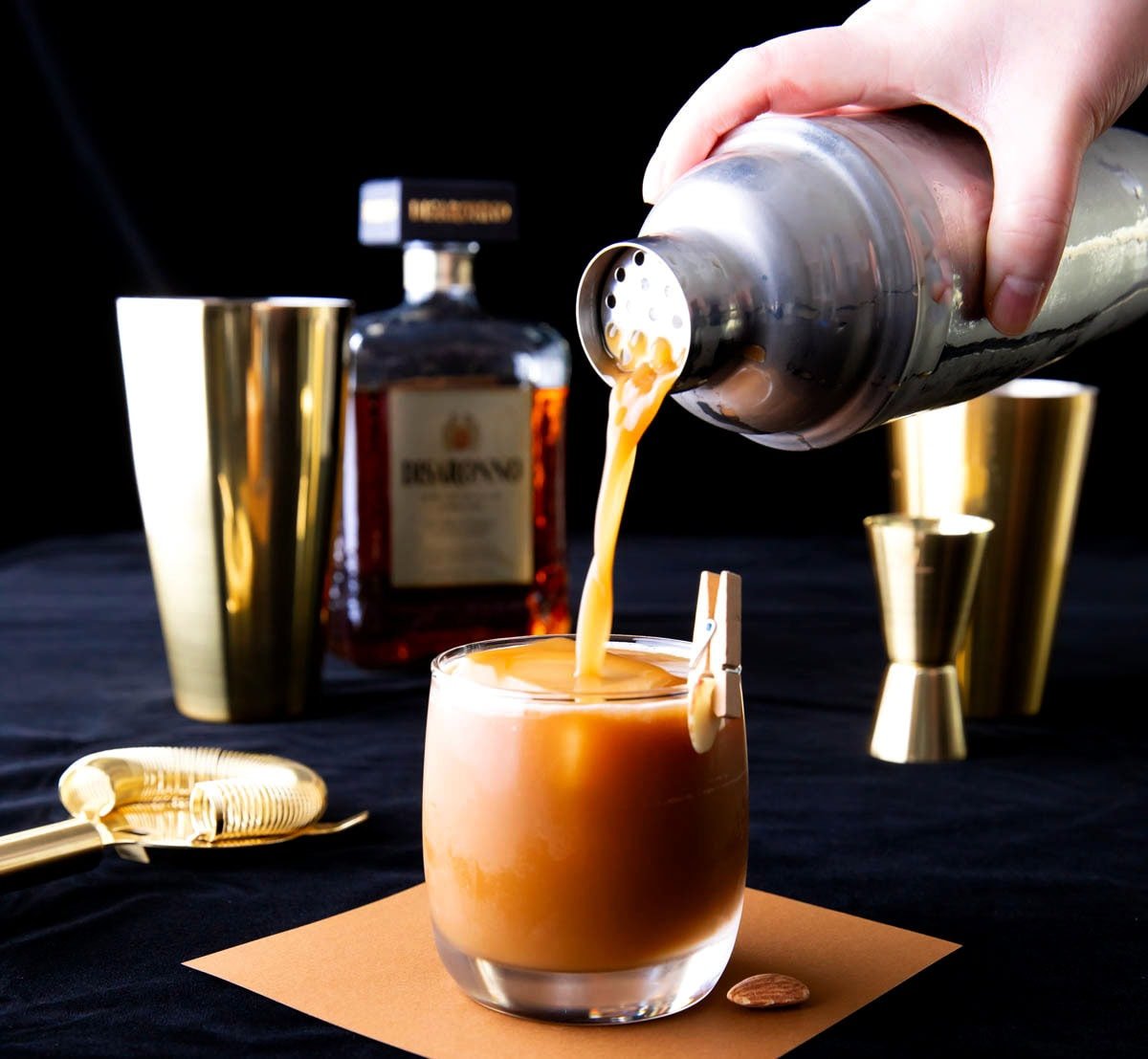 Preparing a Toasted Almond with Disaronno, a gold cocktail shaker, and cocktail tools